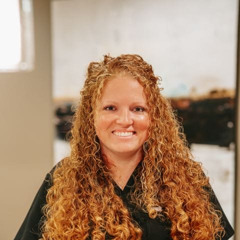 Headshot of Amber Stevenson, Hygienist with bright red curly hair smiles at the camera while wearing black scrubs