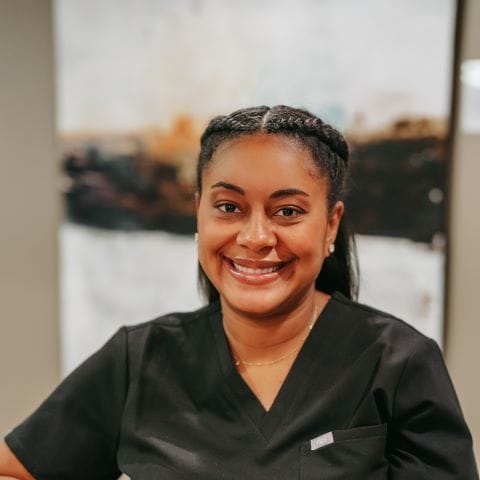 Headshot of Morgan Kiser, Dental Assistant with braided hair smiles at the camera while wearing black scrubs, conveying a caring and approachable dental team atmosphere