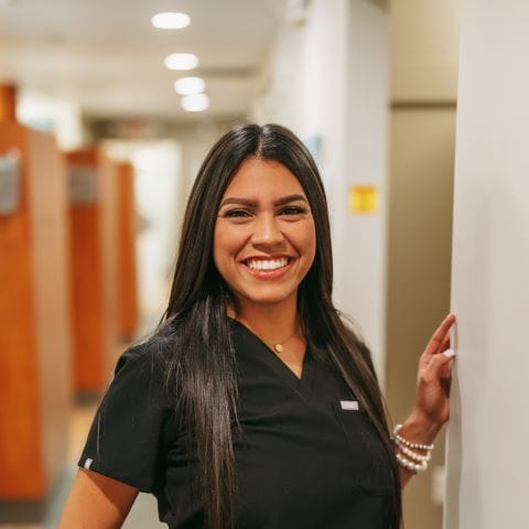 Headshot of Gelieliz Perez-Morales, Dental Assistant with long straight hair smiles brightly in a dental clinic hallway