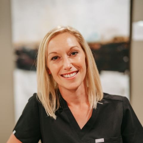 Headshot of Sarah Musgrave, Dental Hygienist in black scrubs smiles warmly inside a well-lit dental office