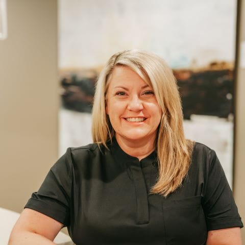 Headshot of Heather Kirby, Practice in black scrubs sits at the reception area, ready to greet patients with a welcoming smile Administrator