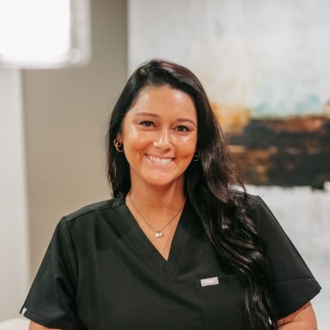 Headshot of Erin Parks, Dental Assistant with long dark hair smiles in a well-lit dental office