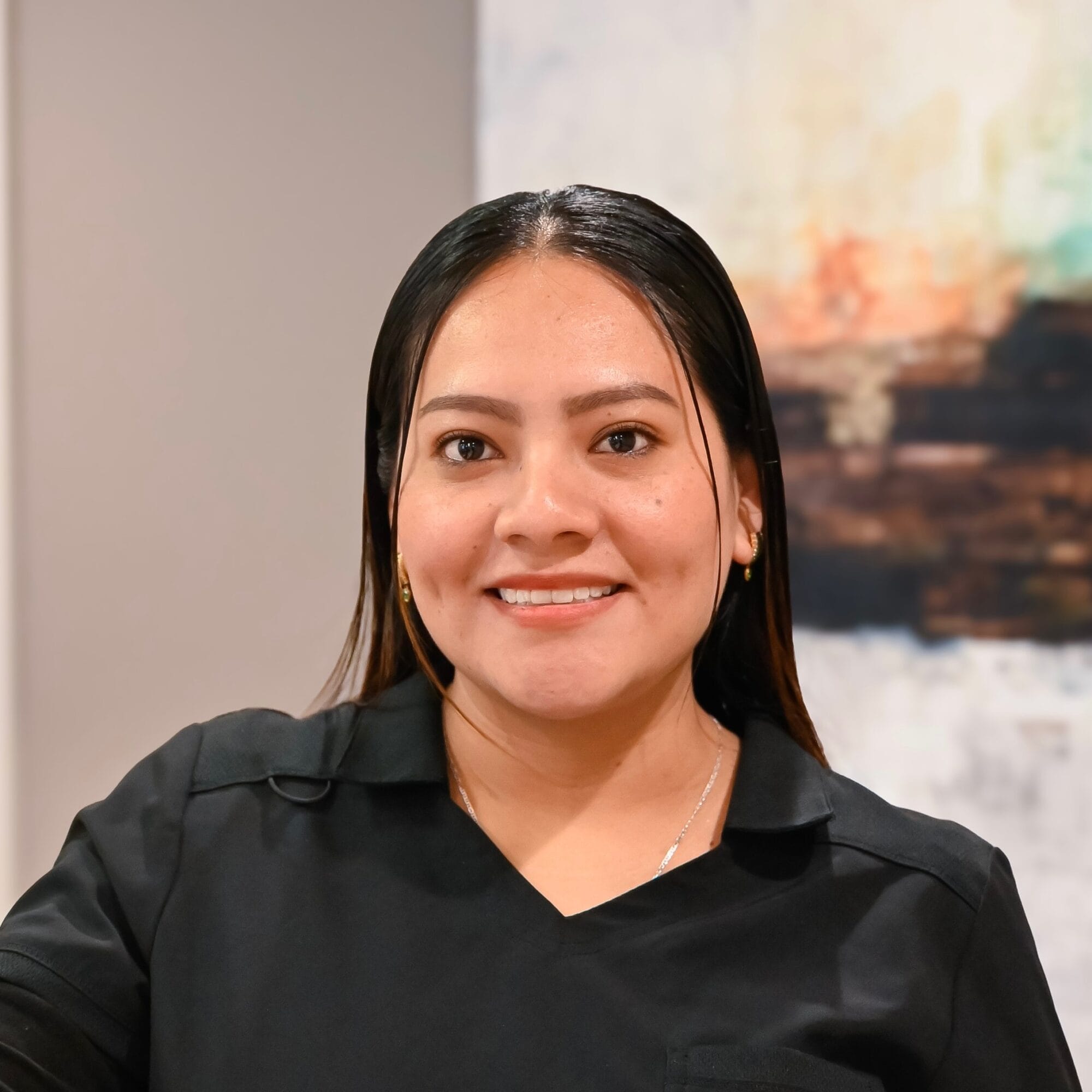 Headshot of Nancy, Dental Assistant in black scrubs smiles confidently in a modern dental office