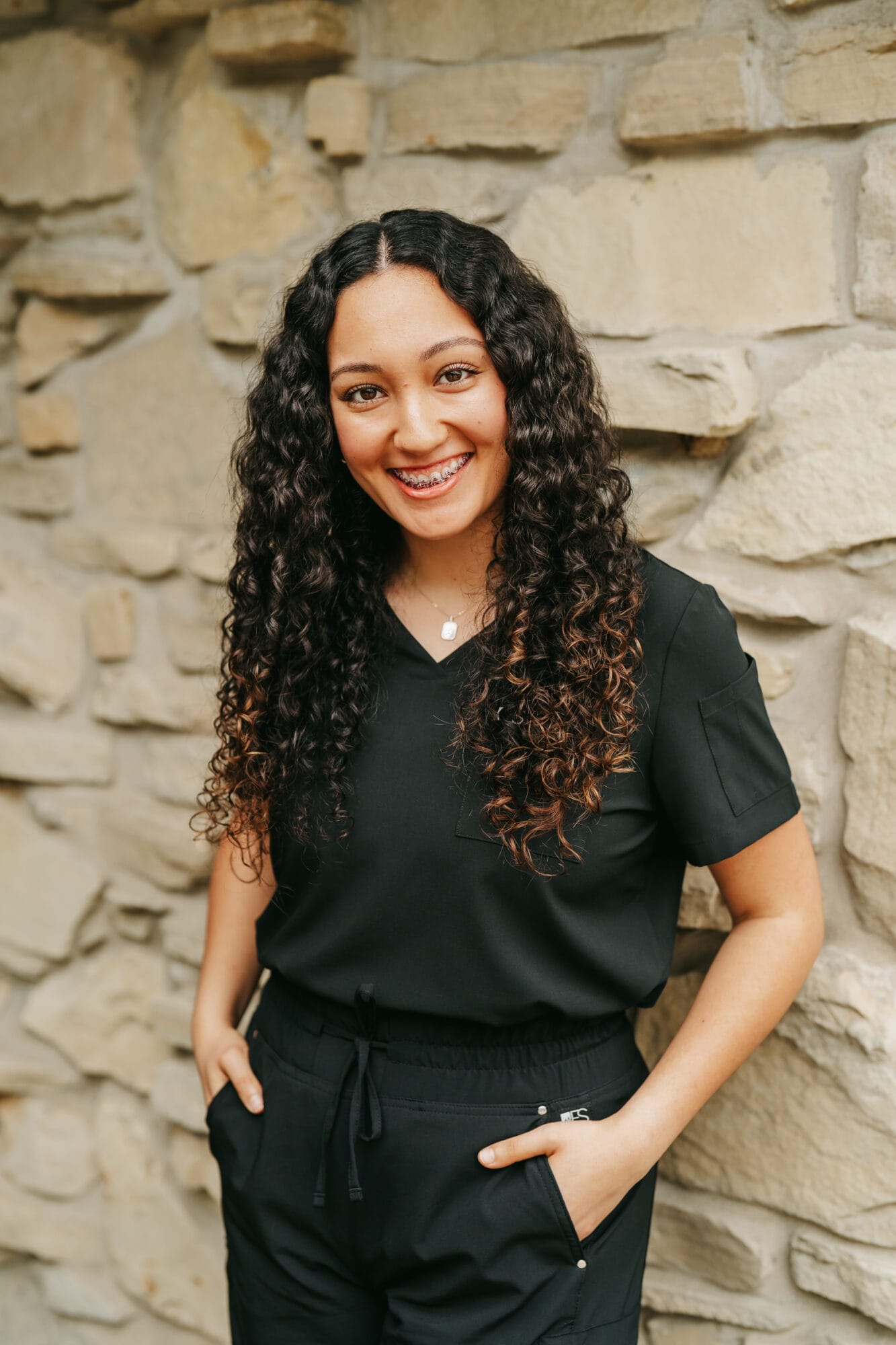 Headshot of Alma Gonzalez, Dental Hygienist with long curly hair stands in a bright dental office hallway