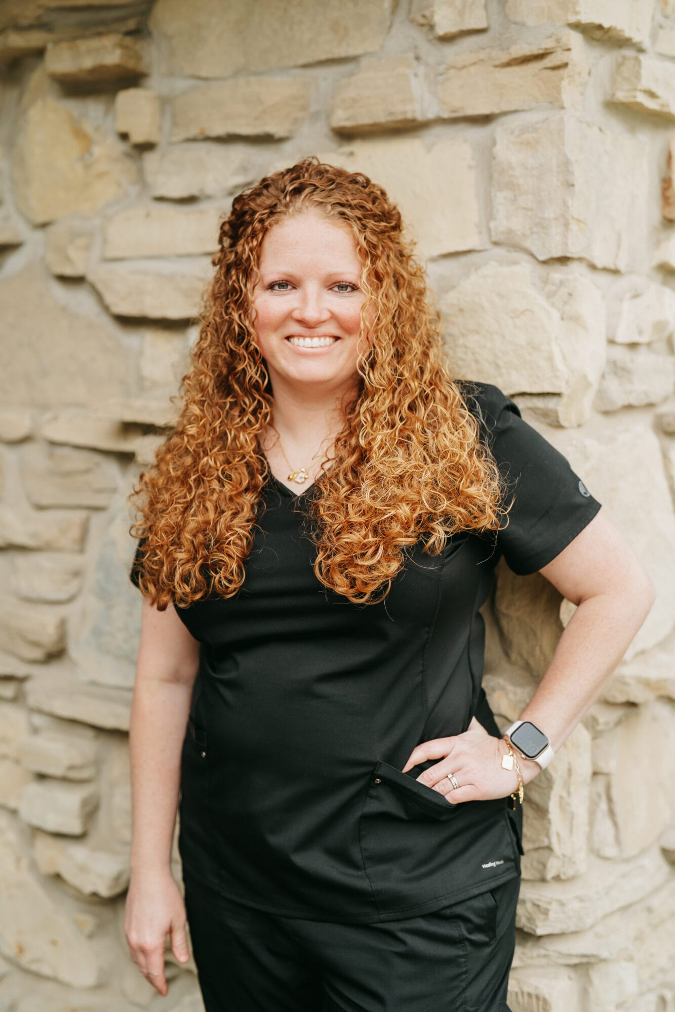 Headshot of Amber Stevenson, Hygienist with bright red curly hair smiles at the camera while wearing black scrubs