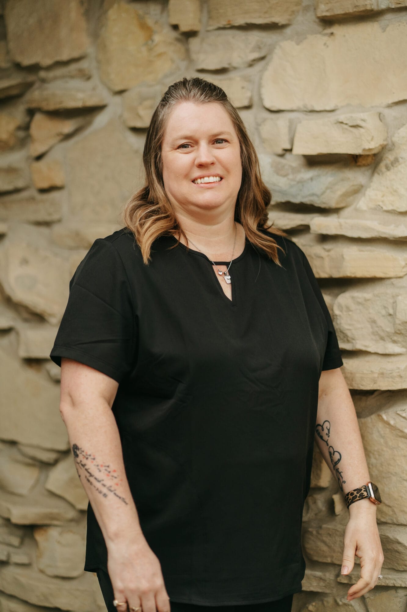 Headshot of Breana Brown, Insurance Coordinator in black scrubs smiles at the camera while sitting at a dental office front desk, conveying professionalism and approachability