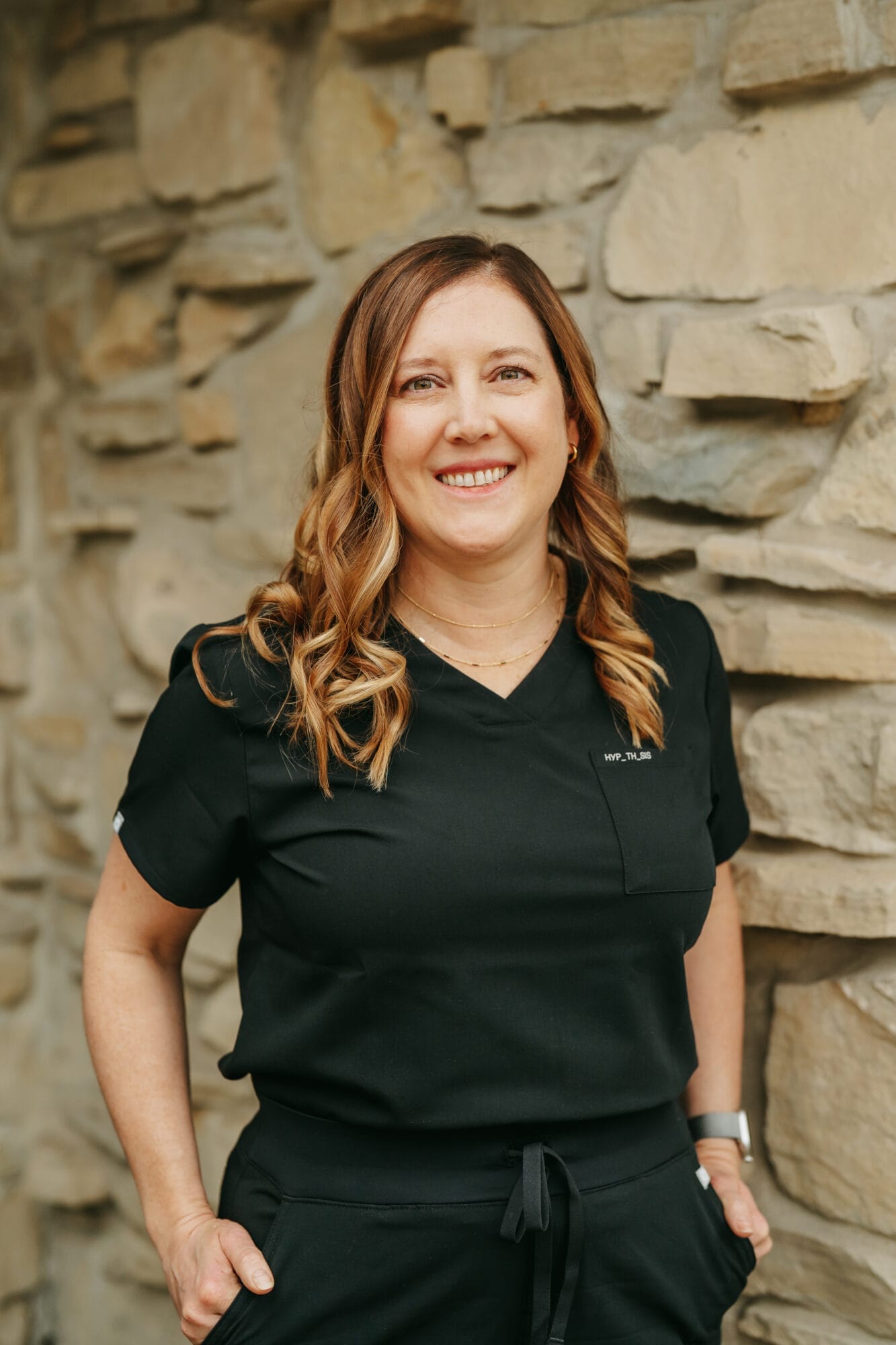 Headshot of Dr. Gabrielle Caron, D.D.S. in black scrubs stands confidently near the front desk of a clean and modern dental office