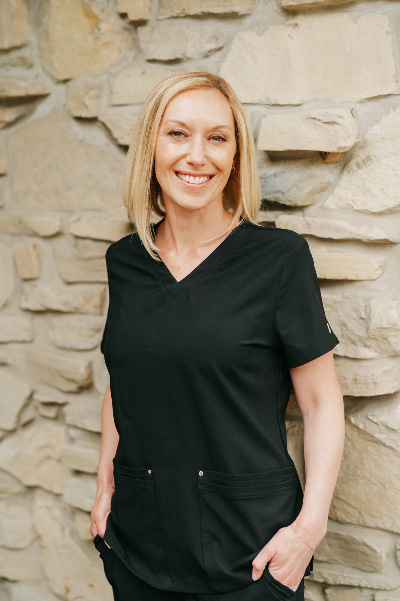 Headshot of Sarah Musgrave, Dental Hygienist in black scrubs smiles warmly inside a well-lit dental office