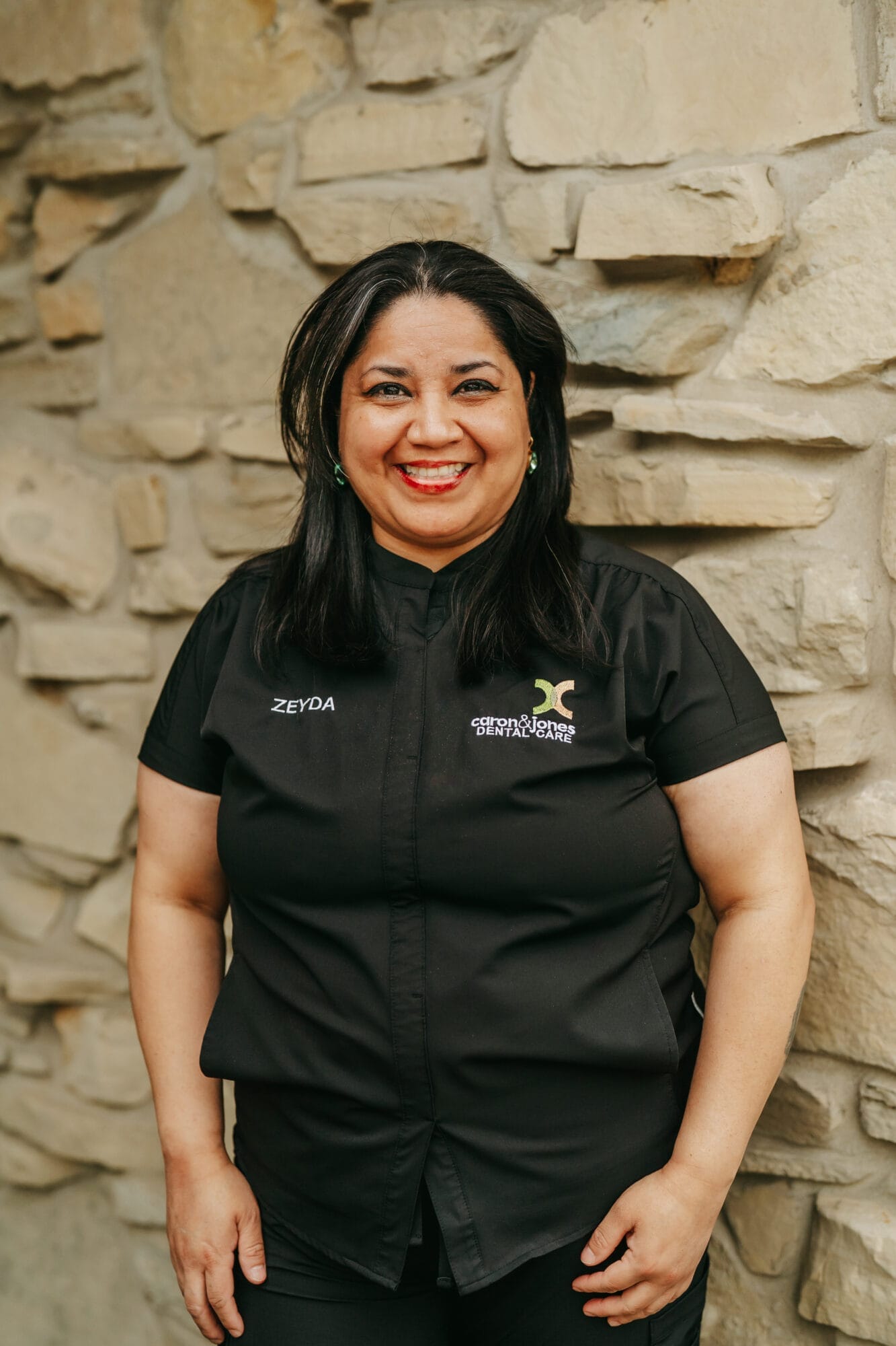 Headshot of Breana Brown, Insurance Coordinator in black scrubs smiles at the camera while sitting at a dental office front desk, conveying professionalism and approachability